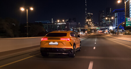 Obraz premium Yellow luxury suv driving on dubai highway at night