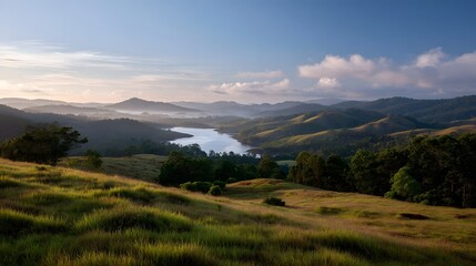 Fototapeta premium A serene landscape of rolling green hills shrouded in morning mist and soft light over a tranquil body of water