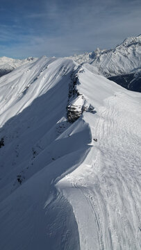 Aerial view of Aiguille Croche mountain ridge covered in deep snow with ski tracks under a clear blue sky in Les Contamines-Montjoie, Auvergne-Rhone-Alpes, France.