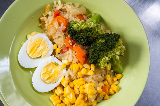 Healthy rice bowl with broccoli sweet corn carrots and hard boiled eggs served on green plate