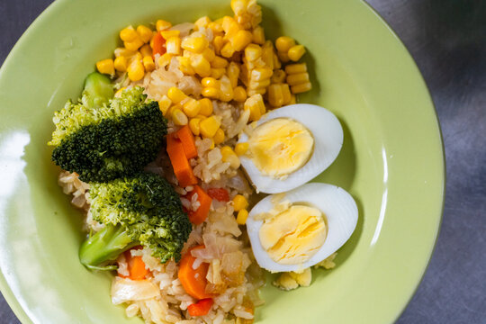Healthy rice bowl with broccoli sweet corn carrots and hard boiled eggs served on green plate