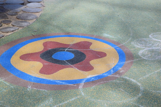 Colorful rubber safety flooring with decorative flower and gear patterns in a children's playground in a city park