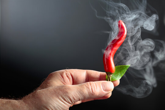 A man's hand holds a steaming hot red chili pepper.