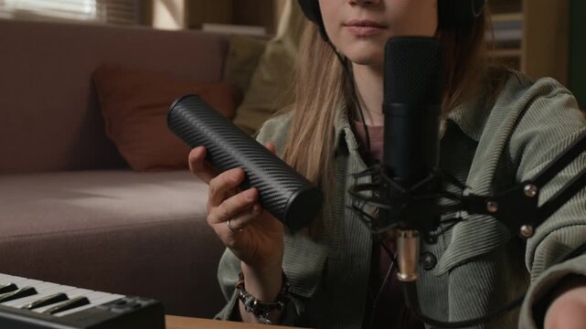 Cropped shot of young female beatmaker recording metal tube shaker sounds through microphone in home studio while creating rhythms in DAW