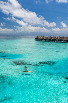 Aerial Maldives turquoise lagoon overwater villas woman paddle boarding recreational outdoors breathtaking dreamy serene luxury resort tropical island Indian Ocean travel destination summer vacation