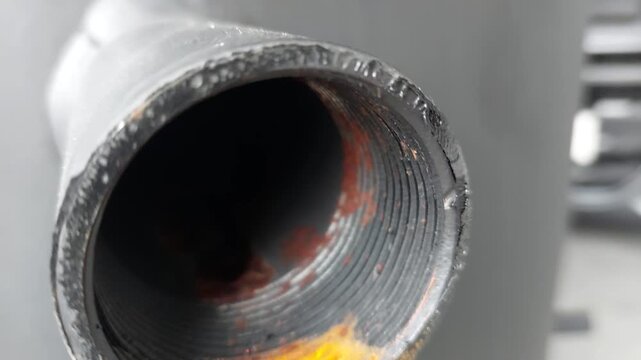 Macro shot of a rusty metal pipe thread on a black industrial tank