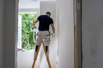 Construction worker standing on ladder while painting and finishing interior apartment wall during professional home renovation project © JairoMZ