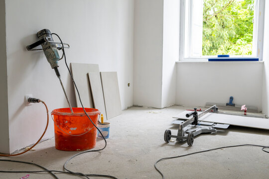 Mixing drill and ceramic tile cutter inside bright unfinished apartment prepared for professional remodeling and interior renovation construction work