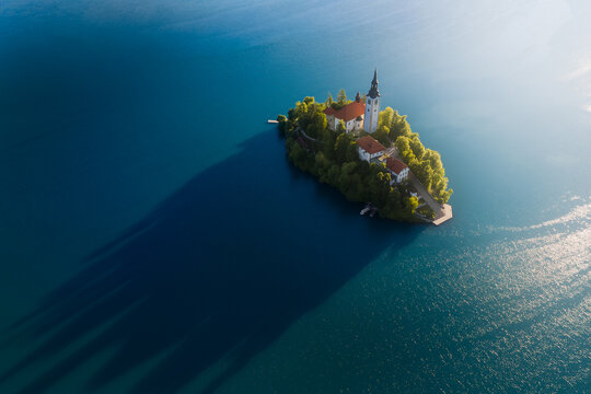 Aerial view of the Pilgrimage Church of the Assumption of Mary on Bled Island surrounded by deep blue water with long morning shadows Bled, Radovljica, Slovenia.