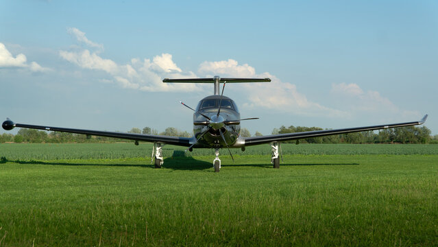 Horizontal photo of a small propeller plane standing on the grass at the airport