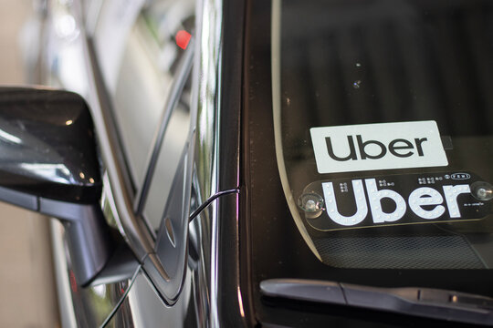 Portland, OR, USA - July 9, 2022: Uber signs attached to the windshield of a car at the designated ride-share pickup area in Portland International Airport.