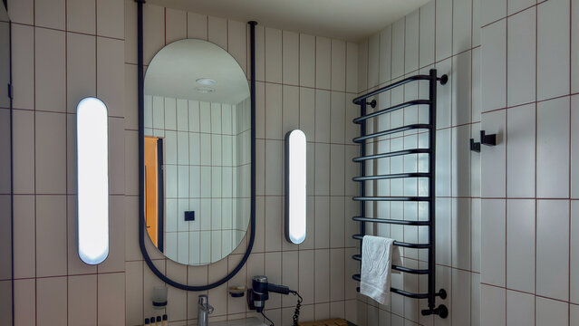 Modern bathroom interior with tiled walls, oval mirror, and black heated towel rail