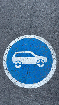 Blue and white circular sign indicating electric vehicle parking on asphalt
