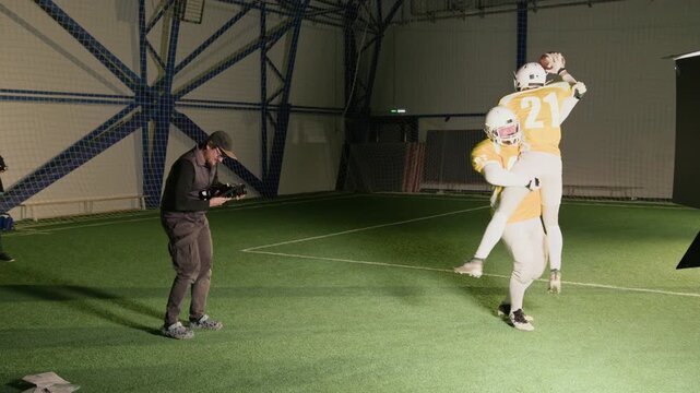 Wide panning shot of cameraman filming gridiron football players in yellow jerseys cheering and hugging after scoring goal during game, while producing content for TV reality show or docuseries