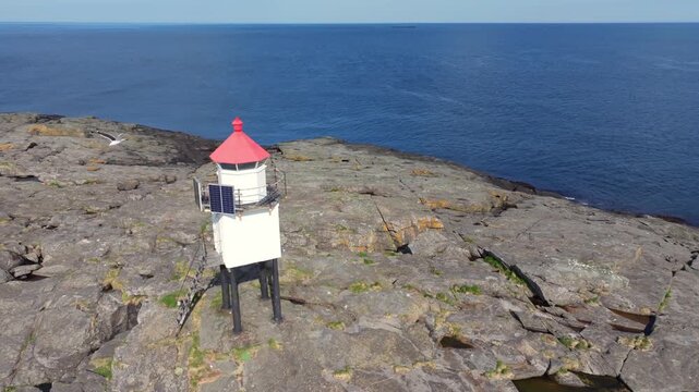Aerial view of the Stromsnes lykt lighthouse, powered by solar panels, standing on a rocky coast on the island of Soroya, Norway