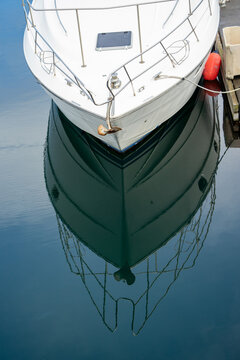 Bow of white yacht reflected in calm marina water, minimal nautical scene with mirror reflection and copy space