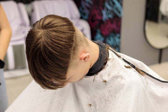overhead view of young boy head showing fresh bowl cut taper fade with cut hair on white cape in modern barbershop with mirror visible