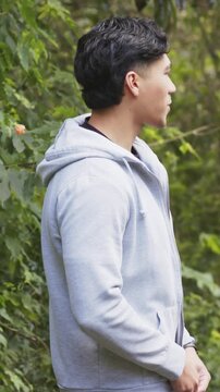 Vertical video: Responding to off-camera voice, man fumbling hoodie zipper and speaking in woods