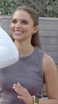 Vertical video: Exchanging high-five, tank-top woman meeting friend entering left on patio, watch