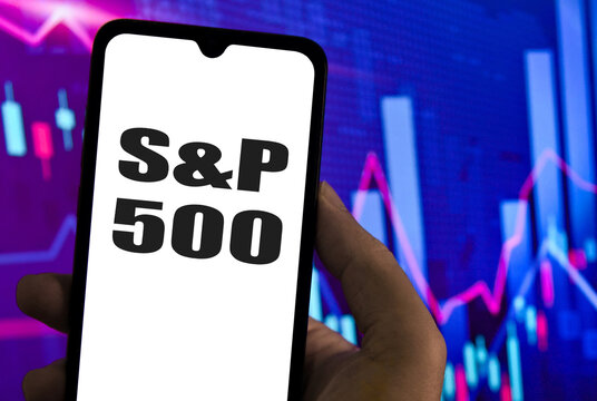 The S&P 500 logo is displayed on a smartphone screen with a stock market chart in the background.. US S&P 500 stock market index value rise or fall on stock exchange. 