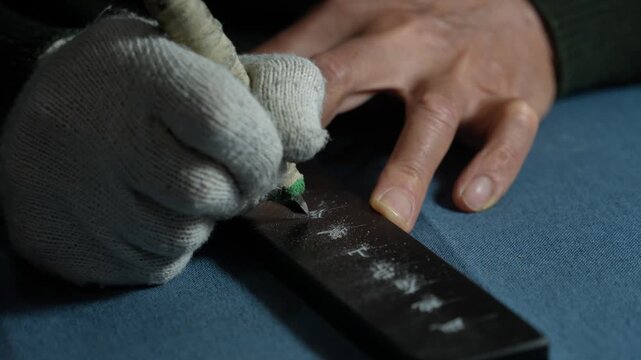 Close-up of a worker wearing gloves polishing a black metal bar with a tool