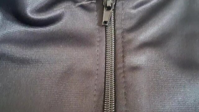 Metal zipper slider moving downward to close the fabric of a black athletic sports jacket