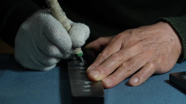 Craftsman wearing gloves holding a tool to engrave a metal plate by hand