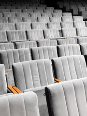 Fototapeta premium Many rows of empty grey seats placed closely together in theater. Armrests of wood neatly aligned in perfect order. Interior of building, empty room, no people, simple minimalistic design