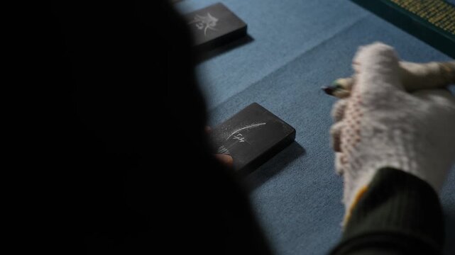 Close-up of a hand wearing gloves holding a calligraphy brush to write