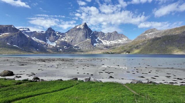 Breathtaking panorama of Morpheus Beach in Lofoten, Norway, with majestic snow capped mountains and a pristine fjord under a cloudy blue sky