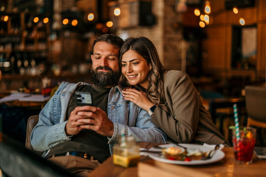 Happy couple relaxing in restaurant using mobile phone
