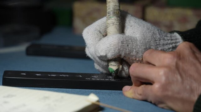 Craftsman wearing gloves holding a carving knife to carve a long wooden block