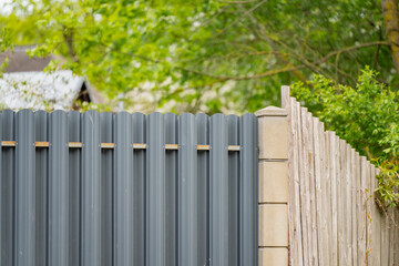 Fototapeta premium Perimeter boundary fencing upgrade showing a new grey metallic corrugated picket section replacing an old rustic wooden plank fence line on a residential property