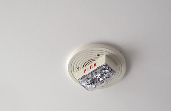 White fire alarm unit mounted on an apartment ceiling featuring speaker and strobe light, with visible &ldquo;FIRE&rdquo; marking as part of building safety system