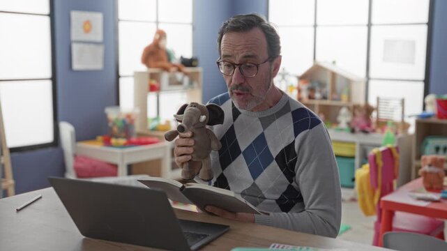 Man holding elephant puppet and open book reads to laptop in building kindergarten classroom with toys and shelves; nurturing warmth.