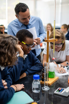 Diverse schoolchildren and a male teacher observe a chemistry experiment