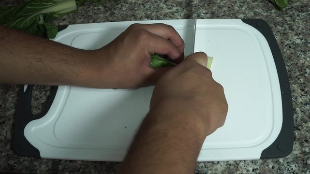 Top view of hands cutting a fresh green chard leaf with a knife on a cutting board
