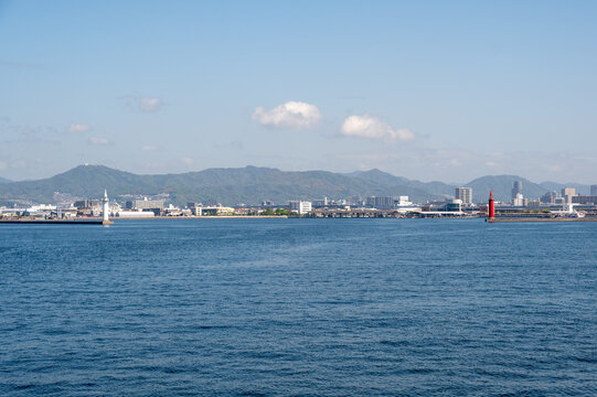 Scenic view of Hiroshima harbor with the white Ujina Lighthouse on a lush green peninsula, Japan