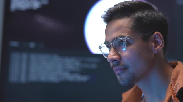 Close up portrait of a focused Asian businessman wearing glasses while tracking core database structures during a late-night software development session.