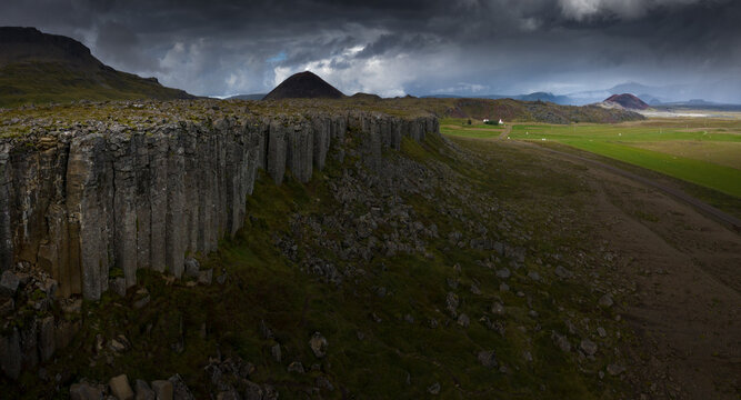 Aerial view of the Gerduberg basalt columns stretching across a rugged landscape with volcanic hills under a dramatic cloudy sky Iceland.