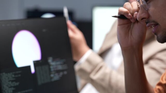 Close up view of tech specialists using a stylus to analyze software source code lines and digital interface graphic elements on a desktop computer monitor.