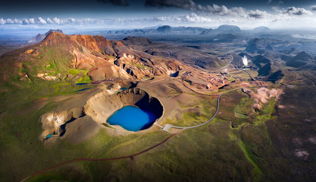 Aerial view of the bright blue Viti crater lake surrounded by rugged volcanic mountains and geothermal steam in the Krafla area, Iceland.