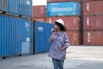 Fototapeta premium asian woman logistics workers walking to check container. operations at a busy shipping container yard. One is holding a tablet while pointing towards the cargo stacks.