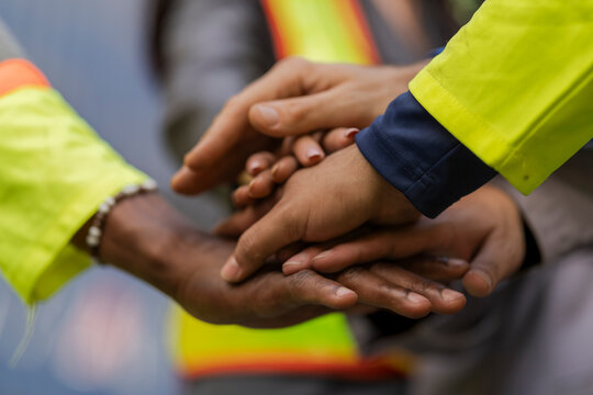 Team logistics workers in high visibility safety gear and hard hats discuss operations at a busy shipping container yard. Team multi nationality working together on site container warehouse.