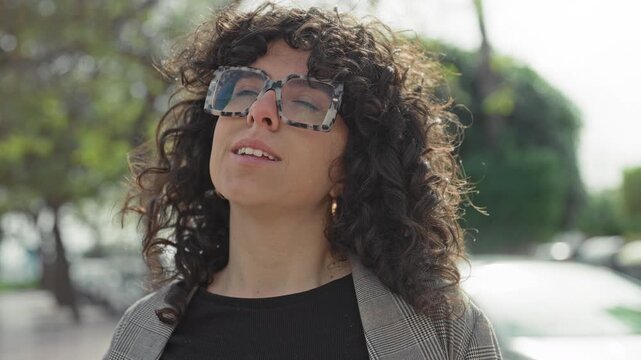 Woman with oversized sunglasses tilting head back exposing face on a sunlit street; serenity reflection.