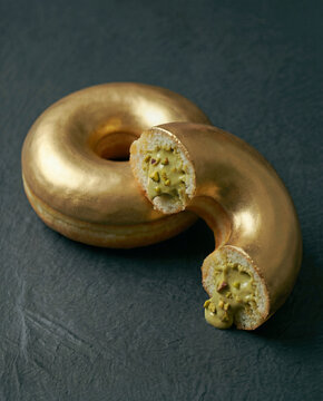Metallic gold glazed baroque donut cut in half with pistachio cream
