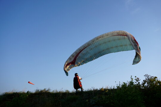 Paraglider pilot preparing for takeoff on a grassy hill against clear blue sky