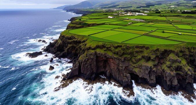 Rocky Atlantic coastline of Azores with green agricultural fields on cliff, aerial view of coastal farmland and ocean waves
