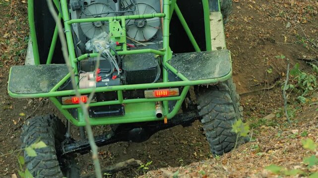 A powerful green off road vehicle descending into a ditch in the forest. A custom-built buggy with a rear-mounted cooling system and large tires. Extreme sports and outdoor adventures
