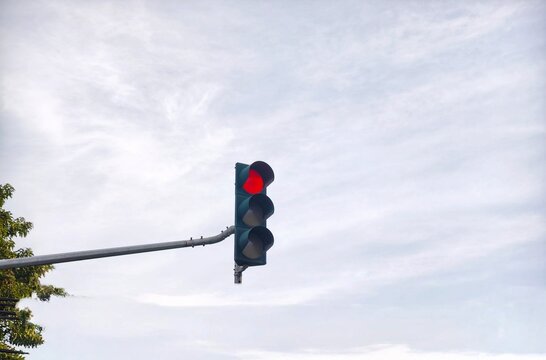 Red traffic light glowing against a bright cloudy sky background in the afternoon. Traffic signal on a metal pole showing stop sign with copy space.